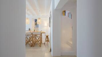 A modern interior with a dining area featuring a wooden table and chairs, pendant lights, and a white wall with a shelf.