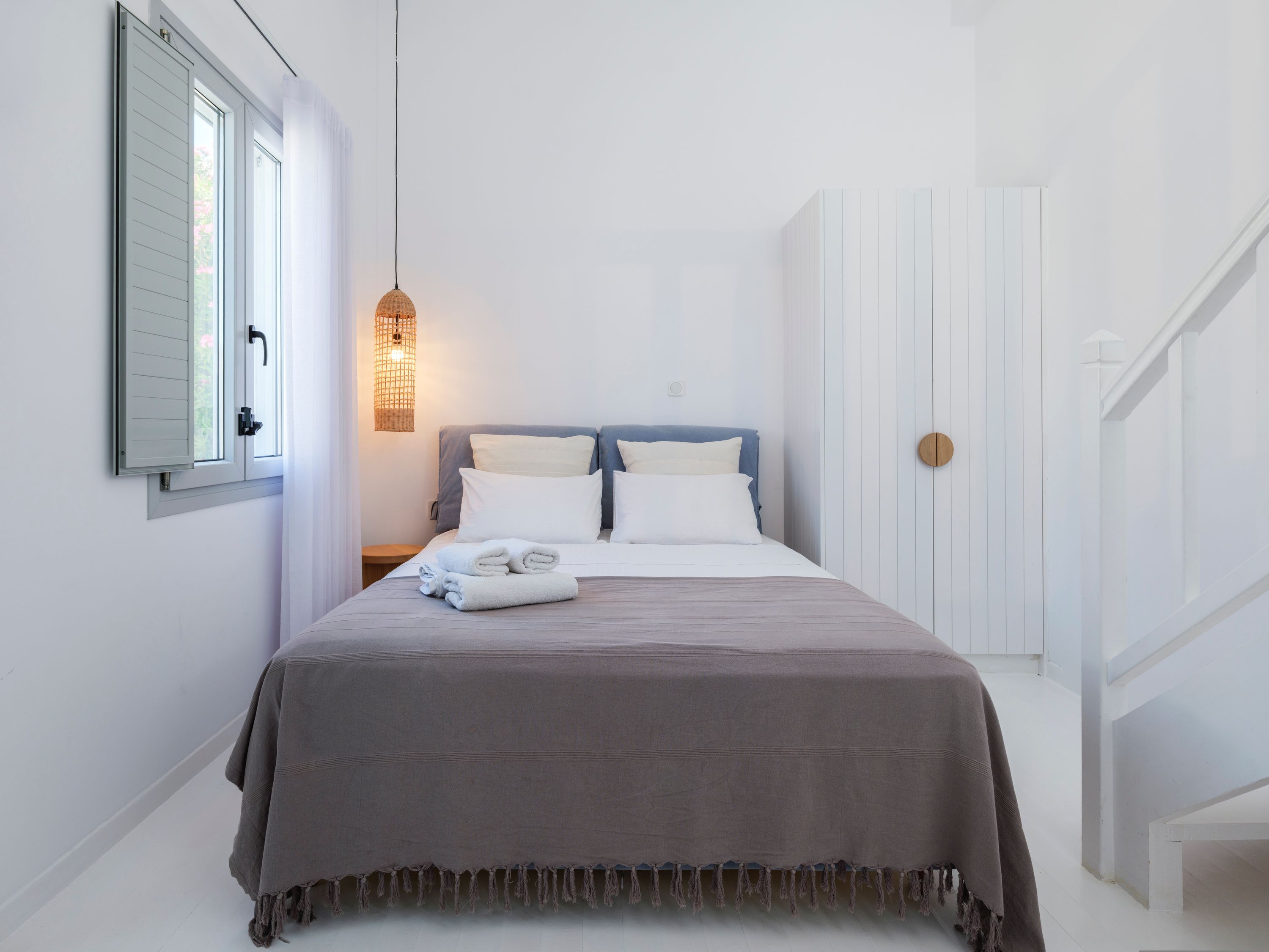 Quarto com cama, almofadas, mesa de cabeceira, luminária pendente e porta.