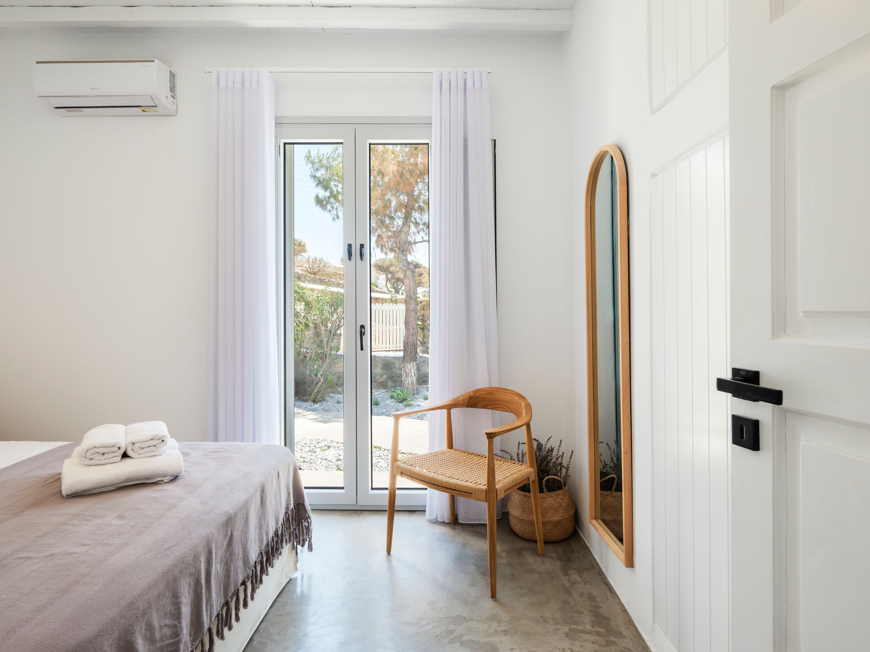 A bedroom with a bed, a chair, a mirror, and a sliding glass door leading to an outdoor area.
