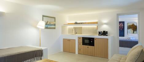 A compact living space with a kitchenette, a sofa, a table, and a lamp.