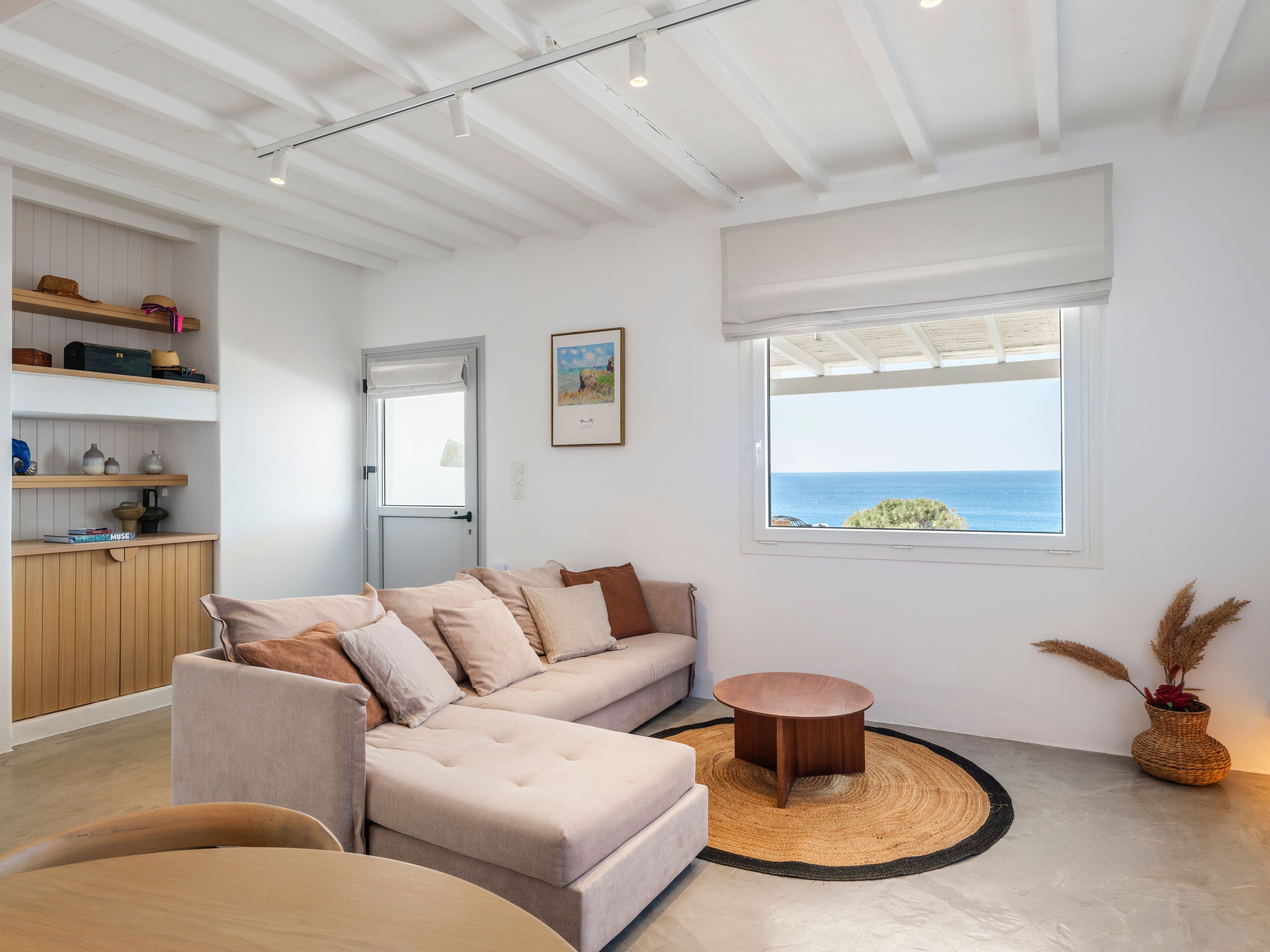 Una sala de estar moderna con un sofá, una mesa de centro redonda y vista al mar a través de una ventana.