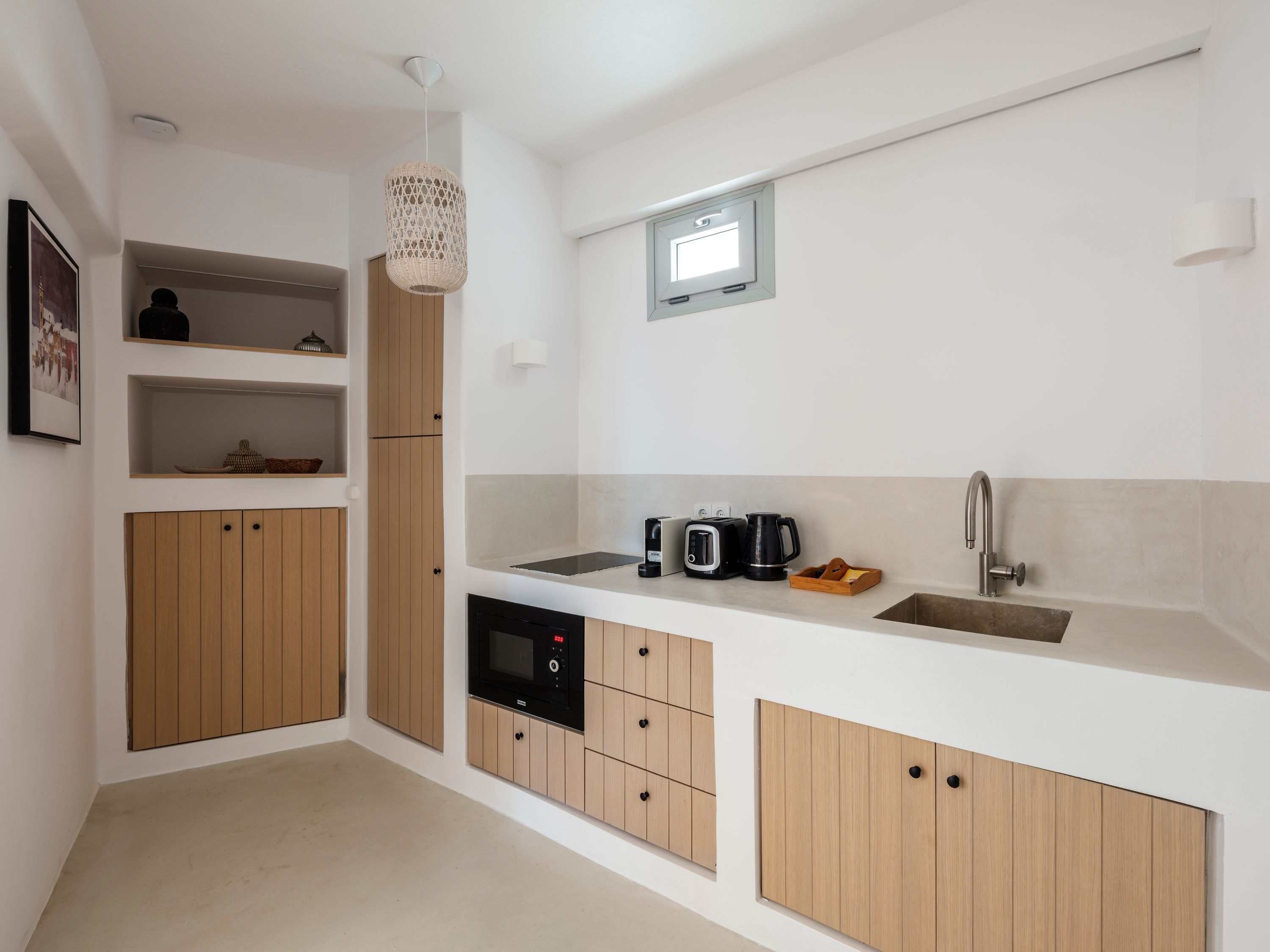 A modern kitchen with wooden cabinets, a built-in microwave, a coffee maker, and a small window.