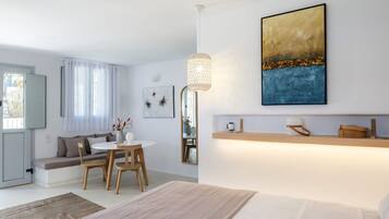 Habitación de hotel moderna con cama, zona de comedor con mesa y sillas, sofá y ventana grande con cortinas.