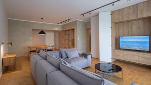 Ein modernes Wohnzimmer mit einem großen grauen Sofa, einem kleinen runden Couchtisch und einem Fernseher auf einer Holzkommode.