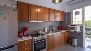 A modern kitchen with wooden cabinets, stainless steel appliances, and a window overlooking a balcony. - Archer - Sea view Apartment (Voula)