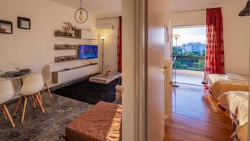 Ein modernes Hotelzimmer mit Essbereich, einem Fernseher, einem Balkon mit roten Vorhängen und Blick auf die Stadt.