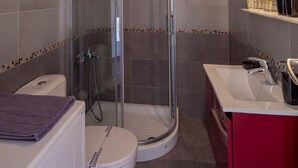 A bathroom with a glass-enclosed shower, a white toilet, and a red vanity with a sink. - Archer - Sea view Apartment (Voula)