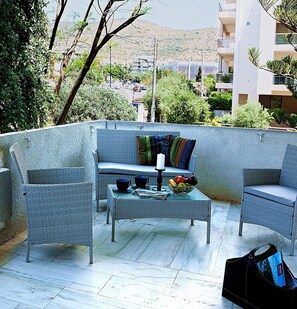 A balcony with wicker furniture, a glass table, and a bowl of fruit. - Aries-Glyfada City Center Apartment (Glifada)