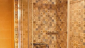 A glass-enclosed shower with a tiled wall featuring a variety of patterns. - Aries-Glyfada City Center Apartment (Glifada)