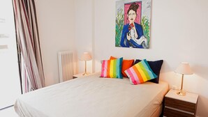 A neatly made bed with a white duvet, colorful striped pillows, and two bedside lamps on wooden nightstands. - Aries-Glyfada City Center Apartment (Glifada)