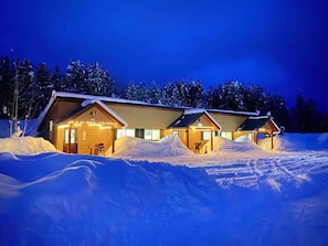 Una baita con pareti in legno, diversi accessi e un paesaggio innevato di notte.
