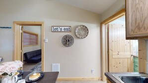 Una cocina con una mesa de comedor, un cartel en la pared que dice 'let's eat' y un plato decorativo.