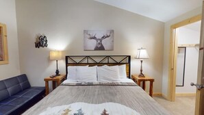 Un dormitorio con una cama, dos mesitas de noche con lámparas, un cabecero, una obra de arte en la pared con un alce, un banco y una puerta.