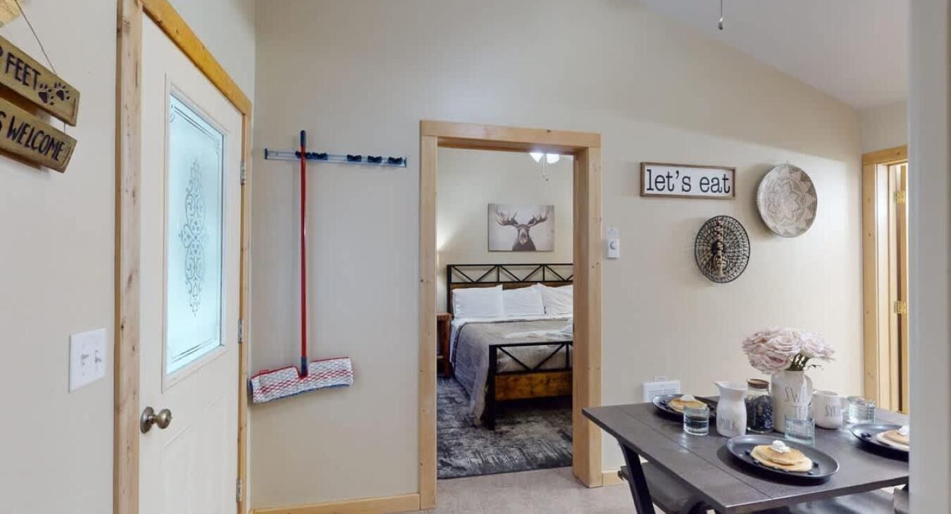 Ein Zimmer mit einem Bett, einem Esstisch mit Tellern und Gläsern, einem Besen und einem Schild mit der Aufschrift 'lasst uns essen'.