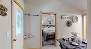 A room with a bed, a dining table with plates and glasses, a broom, and a sign that says 'let's eat'.