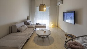 Un salon moderne avec un canapé, une table basse ronde, un fauteuil et un téléviseur fixé au mur.