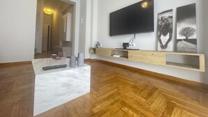 Moderni olohuone, jossa on suuri, seinälle asennettu taulutelevisio, puulattia ja pelkistetty sisustustyyli.