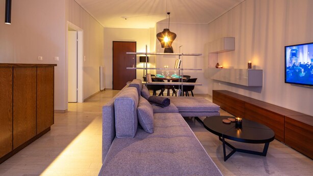 Ein modernes Wohnzimmer mit einer Eckcouch, einem Esstisch mit Stühlen, einem Couchtisch und einem an der Wand montierten Fernseher.