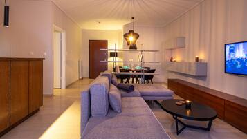 A modern living room with a sectional sofa, a dining table with chairs, a coffee table, and a TV mounted on the wall.