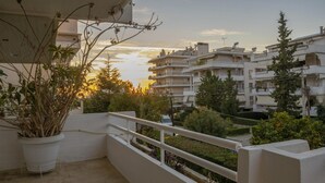 Ein Balkon mit Topfpflanze, weißer Brüstung und Blick auf Wohnhäuser und Grünanlagen bei Sonnenuntergang.