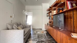 Una sala de estar moderna con un sofá gris, un mueble de madera para entretenimiento con libros y un televisor.