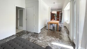 Un pasillo amplio con piso de mármol, un comedor con mesa y sillas, y vista a un baño con bañera.