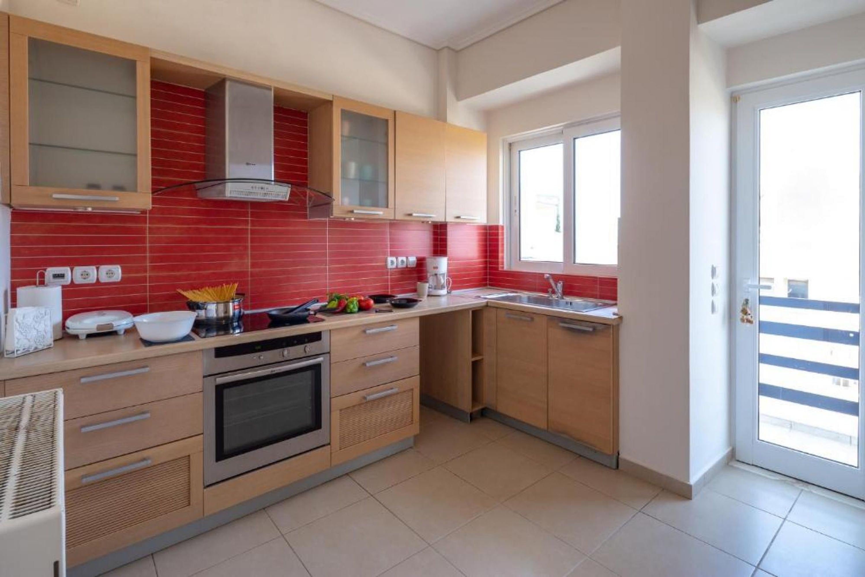 A modern kitchen with wooden cabinets, a built-in oven, and a red-tiled backsplash.