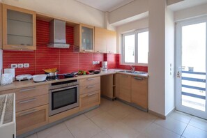 A modern kitchen with wooden cabinets, a built-in oven, and a red-tiled backsplash. - Rhea - Glyfada Sea View apartment (Glifada)