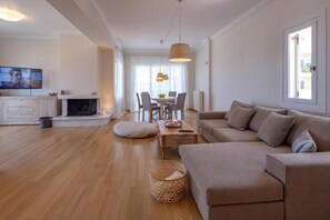 A modern living room with a sofa, a dining table, and a TV. - Rhea - Glyfada Sea View apartment (Glifada)