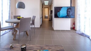 Ein modernes Hotelzimmer mit Essbereich, einem an der Wand befestigten Fernseher und einem Flur zum Schlafzimmer.