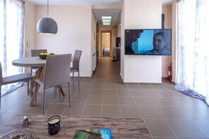 Ein modernes Hotelzimmer mit Essbereich, einem an der Wand befestigten Fernseher und einem Flur zum Schlafzimmer.