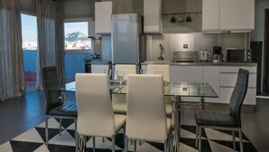A modern kitchen with a dining area, featuring a glass table and chairs, a refrigerator, and a microwave. - Virgo - Loft with Spectacular View to Acropolis (Athina)
