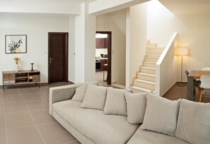 A living room with a beige sofa, a wooden cabinet, a framed picture, and a staircase leading to an upper floor.