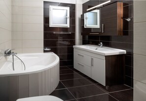 A modern bathroom with a freestanding bathtub, a sink with a vanity, and two wall-mounted mirrors. - Amare Luxury Living Volos (Nees Pagases)