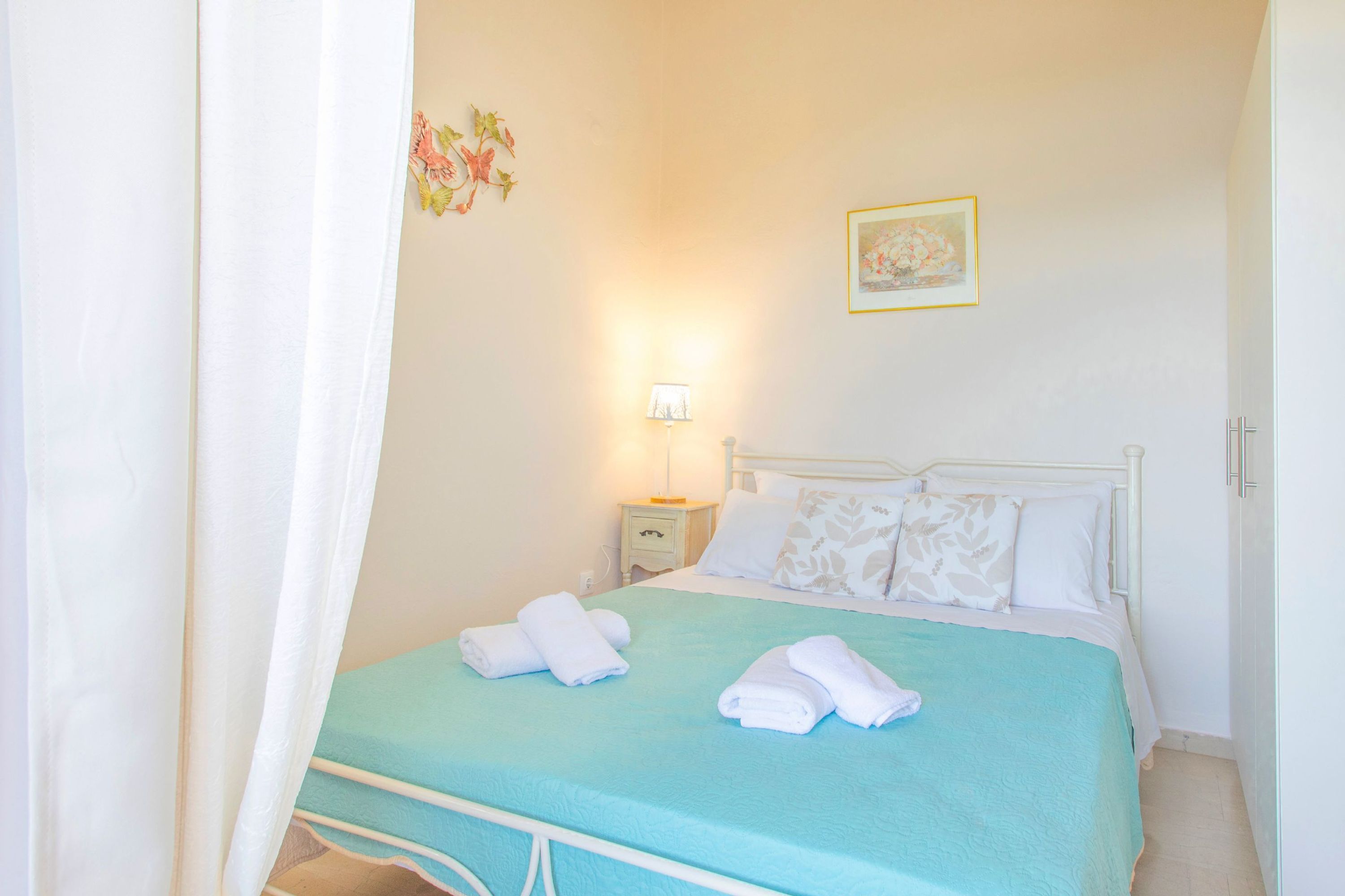 Un lit bien fait, avec du linge de lit blanc et une couvre-lit turquoise, une lampe de chevet et un tableau accroché au mur.