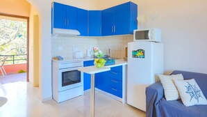 Eine kleine Küche mit blauen Schränken, einem weißen Kühlschrank und einem Essbereich mit einer blauen Couch.