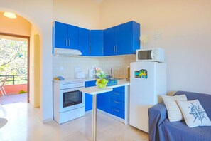 A compact kitchen with blue cabinets, a white refrigerator, and a dining area with a blue sofa. - Evora in Ionian Islands (Ionian Islands)