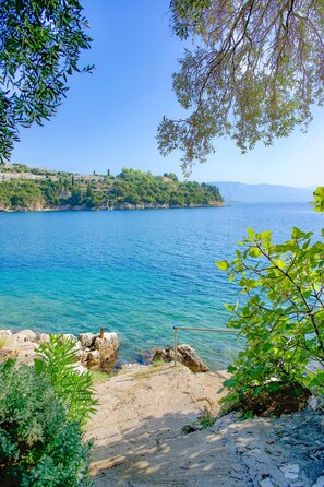A coastal landscape with clear blue water, rocky shore, and greenery. - Evora in Ionian Islands (Ionian Islands)