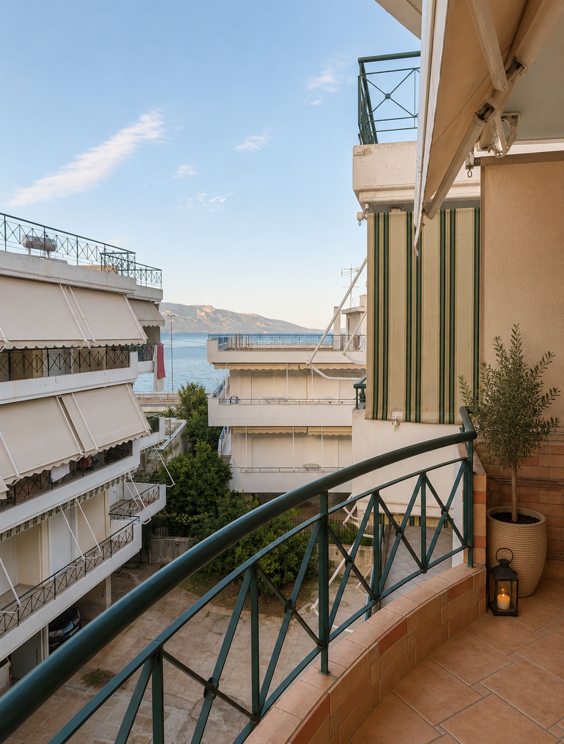 A balcony with a view of the sea, a potted plant, and a tiled floor.