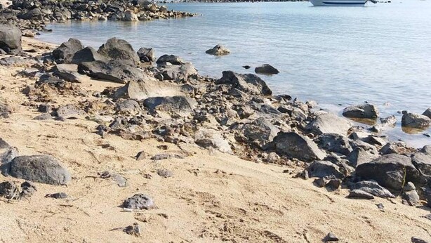 Ein felsiger Strand mit einem Boot im Wasser und Bergen im Hintergrund.