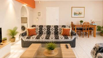 A living room with a sofa, coffee table, dining table, chairs, and a TV.