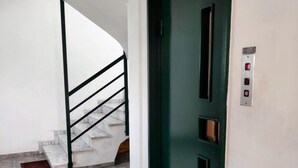 Ein Flur mit einer grünen Tür, einer Treppe und einem Wandbedienfeld für den Aufzug.