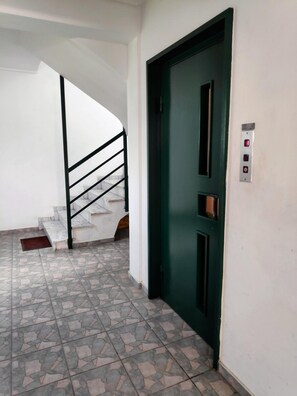Un pasillo con una puerta verde, una escalera y un panel de control de ascensor en la pared.