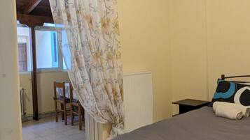 A bedroom with a bed, a chair, a radiator, and a curtain.