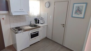 Cocina compacta con armarios blancos, horno empotrado, estufa y hervidor sobre la encimera.