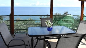 Een terras met een tafel en stoelen, een vaas met bloemen en uitzicht op de oceaan.