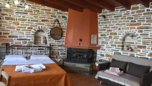 Een kamer met stenen muren, voorzien van een open haard, een bed met een oranje sprei, een bank en een kleine tafel met een spiegel.
