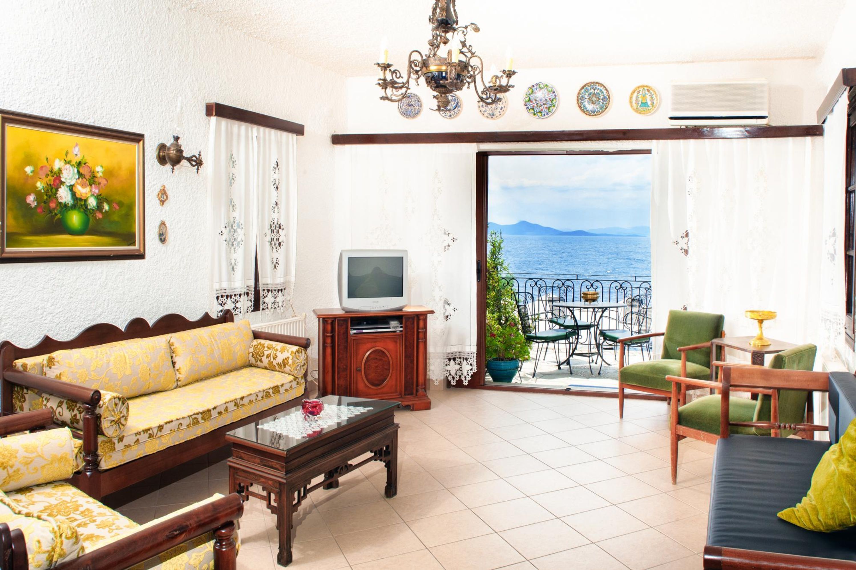 A living room with a sofa, a coffee table, a TV, and a balcony with a view of the sea.