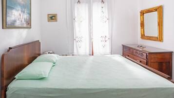 Een slaapkamer met een bed, een dressoir, een spiegel en twee schilderijen aan de muur.