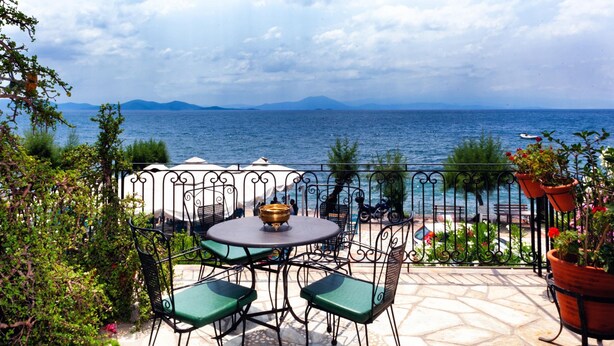 Eine Terrasse mit Tisch und Stühlen, mit Blick auf ein Gewässer und Berge.